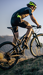 Marca exclusiva Decathlon: Rockrider. Homem com roupas de ciclismo, capacete e sapatilha em sua bicicleta, fazendo trilha.