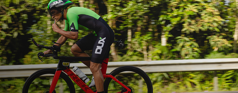 Só na Decathlon online: Homem branco uniformizado com o patrocionio da Dux Nutrition realizando passeio de bicicleta e consumindo um gel de carboidrato para ganho de performance